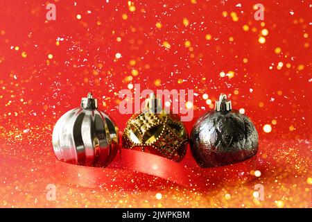 Décorations de Noël boules de couleurs or et argent sur fond rouge avec un ruban rouge satiné et des lumières dorées Banque D'Images
