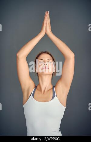 Respirez tout, aimez tout. Une jeune femme pratiquant le yoga sur fond gris. Banque D'Images