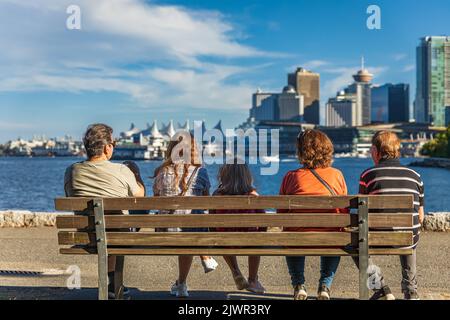 Vue arrière d'une famille de cinq personnes assises sur le banc dans un parc de la ville de Vancouver, C.-B. Canada. Trois générations de famille passant du temps de détente ensemble-se Banque D'Images