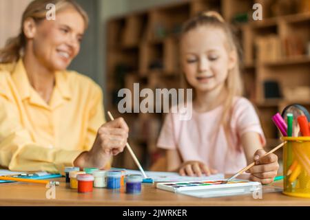 Développement artistique pour les enfants. Petite fille peinture avec professeur à la maternelle, dessin avec des peintures colorées Banque D'Images