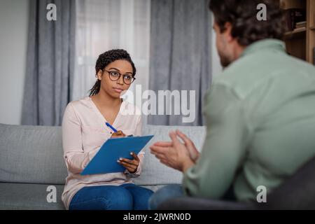 Femme afro-américaine sérieuse millénaire médecin en lunettes Écoutez le triste patient caucasien masculin dans l'intérieur de la clinique Banque D'Images