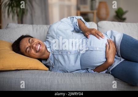 Femme afro-américaine enceinte ayant des contractions douloureuses spasme à la maison Banque D'Images