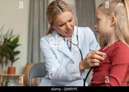 Inquiet pédiatre médecin examinant le rythme cardiaque et les poumons de la petite fille avec stéthoscope, faisant un examen pédiatrique Banque D'Images