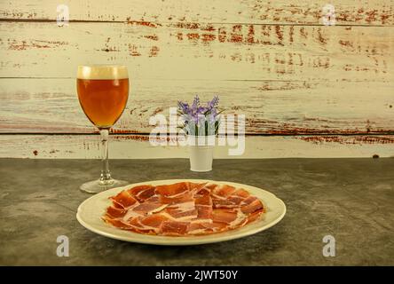 Assiette de jambon Serrano, fraîchement coupée et servie sur une assiette avec un verre de bière. Banque D'Images