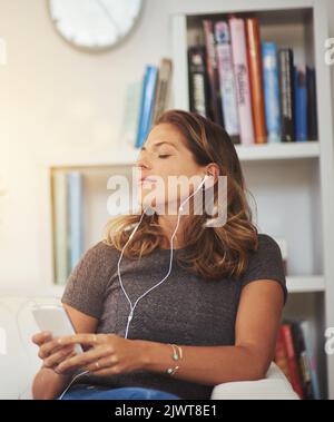 Quand la musique vous parle. Une jeune femme écoute de la musique sur son téléphone à la maison. Banque D'Images