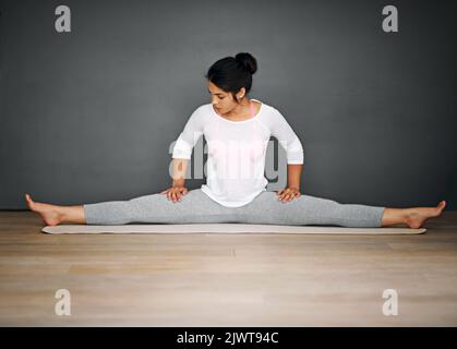 Une jeune femme attirante qui fait les fractionnements de sa routine de yoga fait une bonne séance de musculation. Banque D'Images