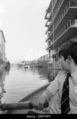 Londres, Angleterre, vers 1967. Un garçon dans un petit bateau qui rame le long du canal Regent's à Camden, en passant par la maison Gilbey sur la droite. Il est membre du Pirate Club. Un autre membre du club navigue sur un canot au loin. Le Pirate Club, un club de canotage pour enfants, a été créé en 1966 à Gilbey’s Wharf, sur le canal Regents, près de Camden, à Londres. Leur pavillon était une ancienne barge et un certain nombre de petits bateaux et de canoës avaient été donnés pour les enfants. Banque D'Images