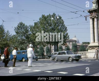 Rome, Italie, 1963. Un policier dirige la circulation sur la Piazza Pasquale Paoli à la jonction de Lungotevere degli Altovitia et du pont Ponte Vittorio Emanuelle II Le pont est nommé en l'honneur de Victor Emmanuel II, roi de Sardaigne entre 1849 et 1861, puis roi d'Italie 1861 jusqu'à sa mort en 1878. Les piétons attendent que le policier arrête la circulation avant de traverser la route. L'Hôpital du Saint-Esprit, le plus ancien hôpital d'Europe, est visible au loin, tout comme le dôme de la basilique Saint-Pierre au Vatican. Un panneau de signalisation indique l'autoroute A2 vers Naples. Banque D'Images