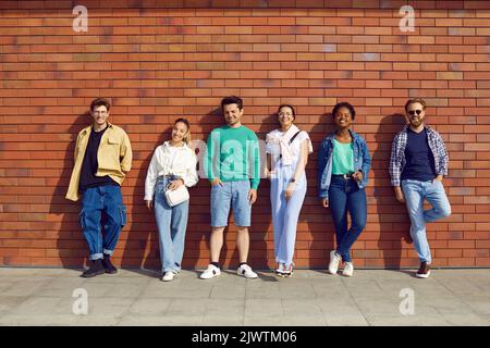 Les jeunes élégants se tiennent dans la rangée et se posent sur fond de mur de briques dans la rue. Banque D'Images
