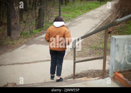 La fille descend les escaliers. Une femme marche dans le parc. Marche le long du chemin. Etudiant dans des vêtements chauds. Banque D'Images