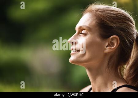 Jeune femme paisible souriant avec les yeux fermés tout en méditant Banque D'Images