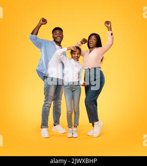 Concept de victoire. Une famille afro-américaine excitée secouant les poings serrés, faisant le geste du gagnant, fond jaune Banque D'Images