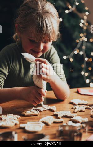 Noël, préparation de la nourriture du nouvel an. Cuisson de pain d'épice de Noël, décoration de biscuits fraîchement cuits avec du glaçage et du mastic. Jolie petite fille décorent le cookie sur une table en bois désordonnée. Bricolage, concept de créativité Banque D'Images