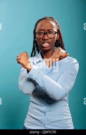Une femme en colère et exaspérée faisant le geste du déclin des bras croisés tout en regardant l'appareil photo. Jeune femme furieuse et irritée qui donne le symbole des mains déclinées sur fond bleu. Banque D'Images
