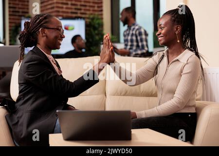 Une équipe de femmes qui donne les cinq grands signes dans le bureau d'affaires, travaillant ensemble sur le rapport de l'entreprise pour créer la présentation. Collaboration et travail d'équipe pour planifier des rapports de données sur ordinateur portable. Banque D'Images