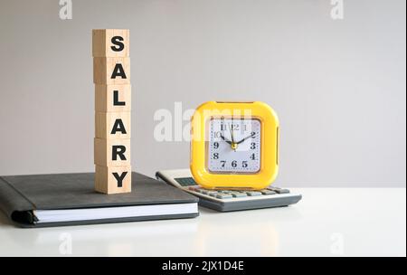 Texte de salaire sur le cube en bois, sur le dessus du bloc-notes et à côté de la calculatrice et de l'horloge. Banque D'Images