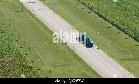 Une vue aérienne en haut regardant un transporteur de voitures sur la route quittant une usine automobile, transportant des voitures nouvellement fabriquées. Banque D'Images