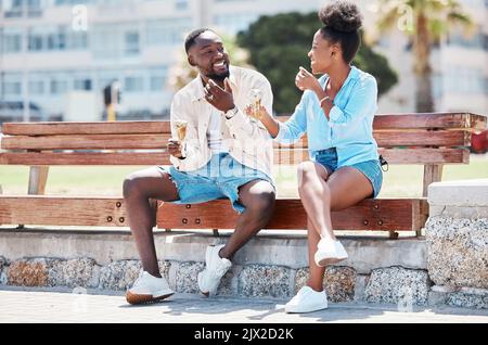 Joyeux couple noir mangeant de la crème glacée sur un banc de plage ensemble, souriant tout en liant et en riant. Jeune Afro-américain homme et femme appréciant leur Banque D'Images