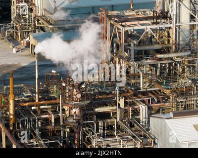 Une vue rapprochée de la tuyauterie industrielle complexe d'une raffinerie de pétrole est vue sous la lumière du matin comme une cheminée d'échappement en fonctionnement. Banque D'Images