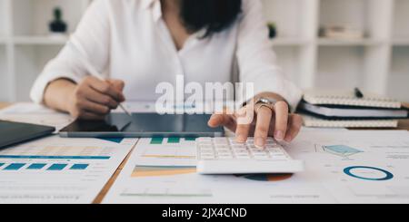 Asian Business Woman ou Accountant font des mathématiques et des analyses avec la calculatrice et la paperasserie sur le bureau, compte, audit et le concept d'épargne Banque D'Images