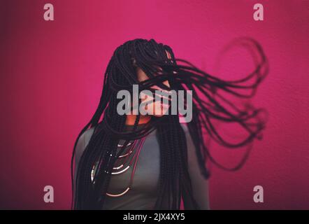 Shes balançant cette coiffure. Une jeune femme avec des tresses posant sur un fond rose. Banque D'Images