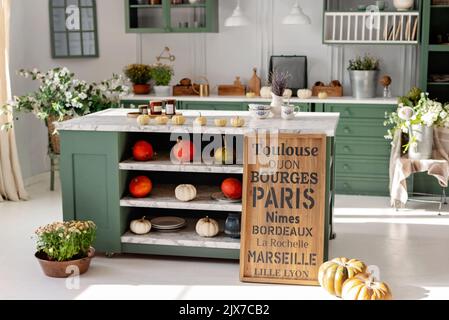 Cuisine avec mobilier vert vintage, suspensions, comptoir en marbre avec fleurs et citrouilles, pots de fleurs d'automne, armoire avec plusieurs tasses Banque D'Images