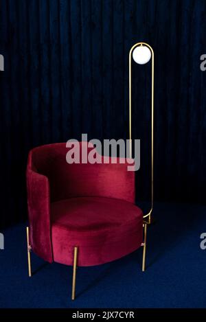 Cette chambre comprend un confortable fauteuil en velours rouge, un lampadaire minimaliste dans le salon avec des panneaux muraux en velours bleu foncé et de la moquette. Banque D'Images