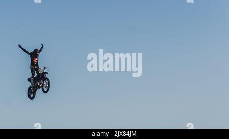 Prise de vue panoramique d'une moto extrême sautez dans les airs. Conducteur de vélo dans un équipement de protection debout sur le vélo et bras d'étirement en l'air. Ciel bleu comme arrière-plan uniforme et sans couture. . Photo de haute qualité Banque D'Images
