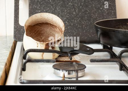 Turk sale du café se trouve sur une cuisinière à gaz dans la cuisine avec du café renversé, du café du matin, des carreaux sales Banque D'Images