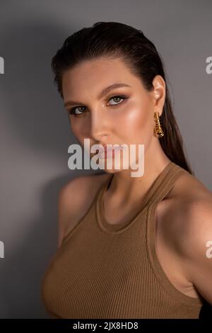 Vue latérale d'une jeune femme assurée et bien entretenue avec de longs cheveux foncés, un maquillage brillant, portant des boucles d'oreilles dorées. Banque D'Images