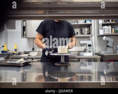 Décorateur à l'aide d'une spatule et d'un grattoir pour lisser la crème de  beurre sur un gâteau dépoli Photo Stock - Alamy
