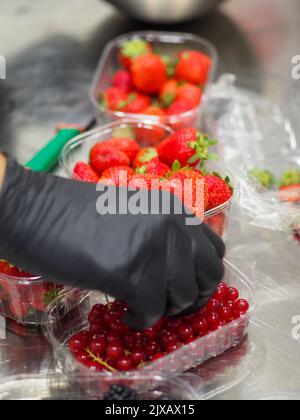 Chef coupant des baies en cuisine, porte des gants noirs pour l'hygiène Banque D'Images