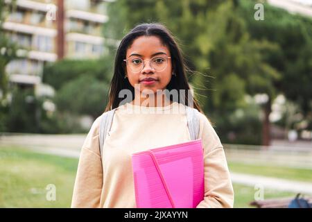 Un adolescent hispanique sérieux debout à l'extérieur à l'université capus regardant la caméra avec ses googles. Portrait de jolie fille d'école. Banque D'Images