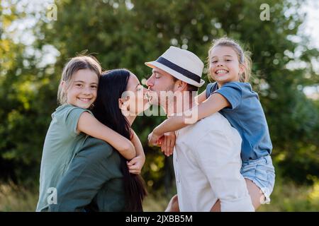 Portrait de jeune couple avec leurs filles dans la nature, embrassant. Vue latérale. Banque D'Images