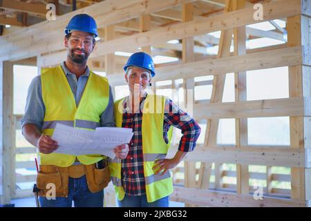 Des ingénieurs de construction ou des architectes avec des plans-plans visitant le site de construction écologique de la maison de cadre en bois Banque D'Images