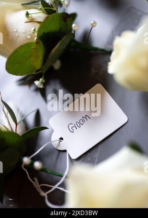 L'étiquette du marié sur la fleur en relief de mariage favorise la fleur à attacher au groomsman à la célébration. Fleurs roses à bord en attente d'être portées. Banque D'Images