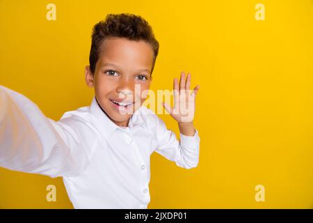 Photo de joli garçon drôle distance leçon main vague camarades de classe amis disent hi vide espace isolé sur fond jaune couleur Banque D'Images