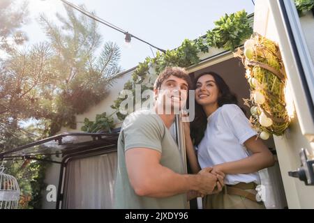 Vue à faible angle du couple souriant tenant les mains près de la porte de la camionnette de camping à l'extérieur, image de stock Banque D'Images