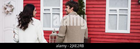 Vue latérale de couple gai en cardigans tricotés regardant les uns les autres près de la maison, bannière, image de stock Banque D'Images