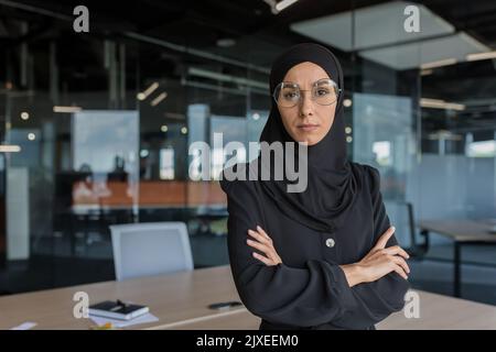 Portrait d'une femme boss dans le hijab, femme d'affaires sérieuse et concentrée travaillant à l'intérieur d'un immeuble de bureau moderne, femme employée avec des bras croisés regardant la caméra. Banque D'Images