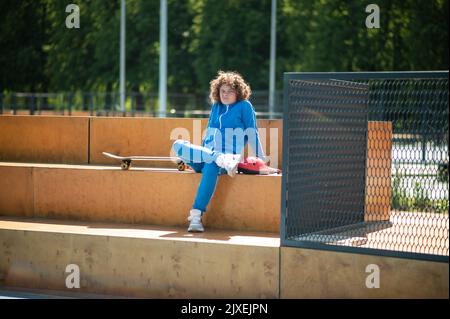 Adolescent fatigué dans le costume de sport assis à l'extérieur Banque D'Images