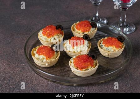 Tartelettes festives au caviar rouge, aux œufs et au fromage fondu, décorées d'olives noires sur une assiette ronde Banque D'Images