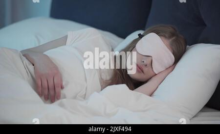 Jeune femme dans le masque de sommeil couché sur le lit la nuit, image de stock Banque D'Images