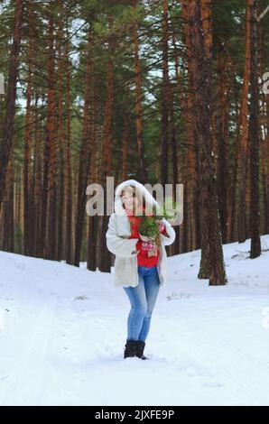 drôle de vieille femme en jeans, chapeau blanc et veste dans le parc neigeux, forêt. Mère marchant près de pins couverts de neige. Amuse-toi bien. Hiver en famille Banque D'Images