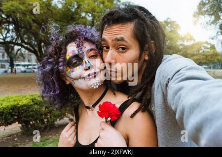 couple hétérosexuel regardant l'appareil-photo appréciant de prendre un selfie dans le parc le jour des morts, téléphone perspective. Banque D'Images