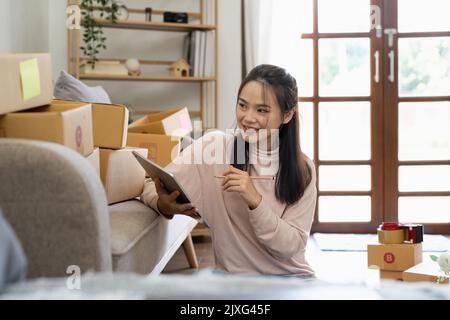 Jeune souriant belle propriétaire asiatique femme freelance pme commerce en ligne travail sur ordinateur portable avec boîte à colis sur le lit à la maison - PME Banque D'Images