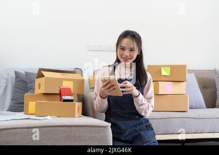 Jeune souriant belle propriétaire asiatique femme freelance pme commerce en ligne travail sur ordinateur portable avec boîte à colis sur le lit à la maison - PME Banque D'Images