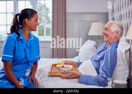 Femme travailleur de soins en uniforme amener l'homme senior à la maison petit déjeuner au lit sur plateau Banque D'Images