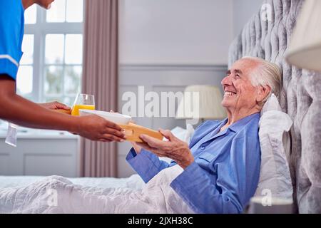 Femme travailleur de soins en uniforme amener l'homme senior à la maison petit déjeuner au lit sur plateau Banque D'Images