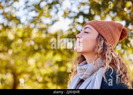 Calme jeune femme portant un chapeau et un foulard se détendant et respirant profondément dans le parc d'automne Banque D'Images